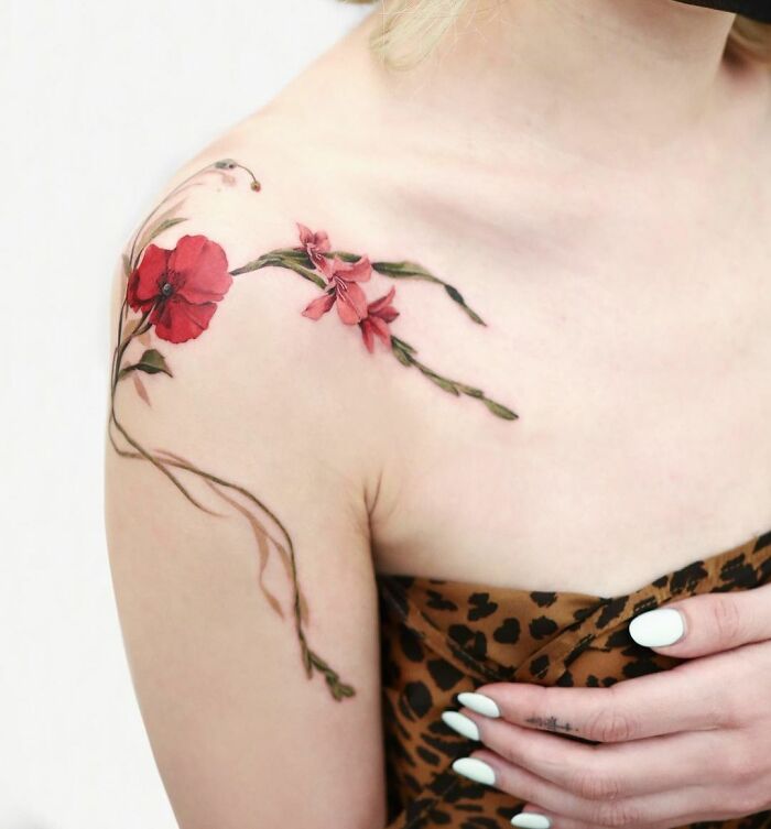 Red floral collarbone tattoo on a woman's shoulder, featuring delicate poppy and vine design.