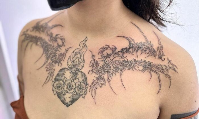 Intricate collarbone tattoo featuring a flaming heart with ornate floral and thorn design.