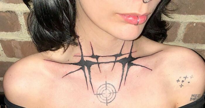 Collarbone tattoos on a person featuring geometric and pointed designs, with a unique target symbol in the center.