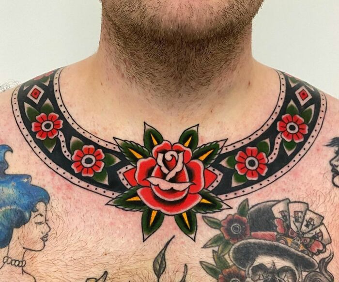 Ornate collarbone tattoo featuring a bold red rose and floral patterns.