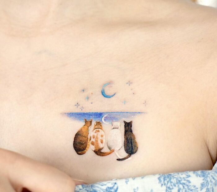 Collarbone tattoo featuring four cats gazing at a crescent moon and stars.