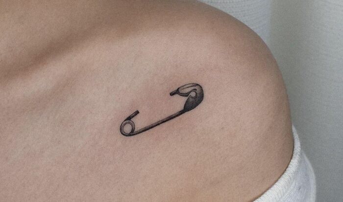 Collarbone tattoo of a safety pin on a person's shoulder, showcasing a minimalist design for men and women.