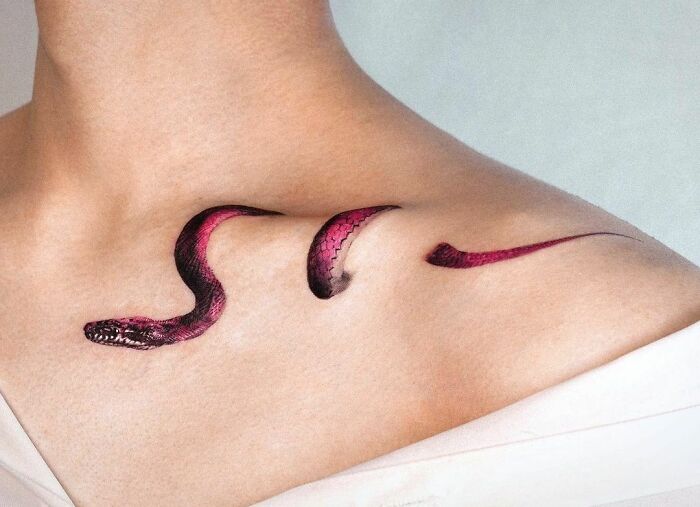 Snake collarbone tattoo in red and black on a person's upper chest.