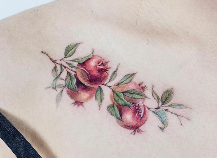 Pomegranate branch collarbone tattoo with leaves, showcasing detailed and vibrant design for men and women.