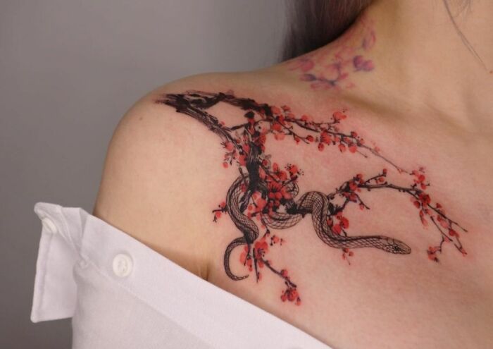 Collarbone tattoo of a snake intertwined with cherry blossoms on a woman's shoulder.
