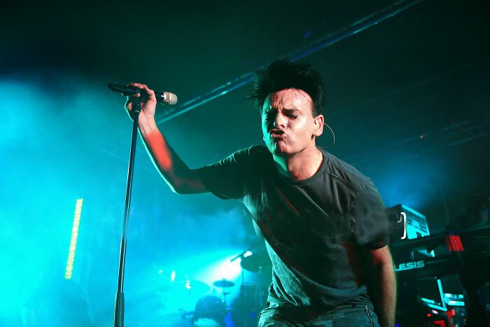 Singer performing energetically on stage with microphone, captured during a live concert with dramatic lighting, weird facts vibe.