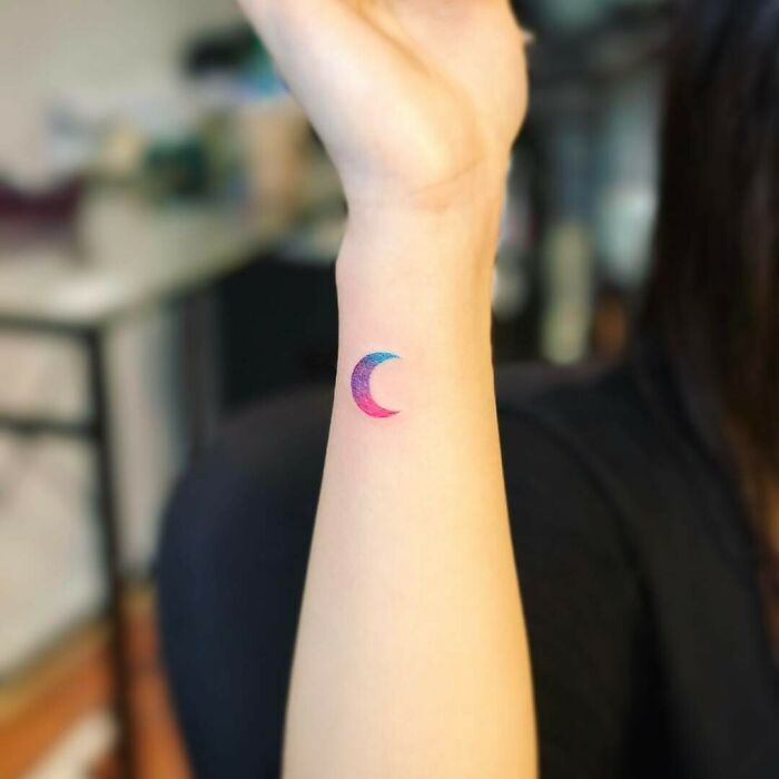 Colorful crescent moon wrist tattoo design, blending shades of pink and blue.