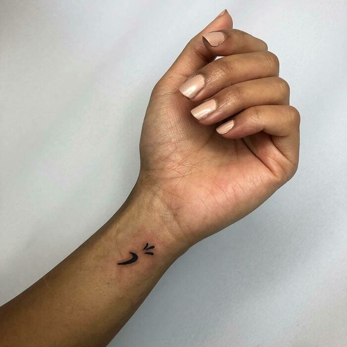 Minimalist wrist tattoo of a small smiling face on forearm.