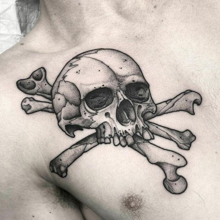 Collarbone tattoo featuring a detailed skull and crossbones design.