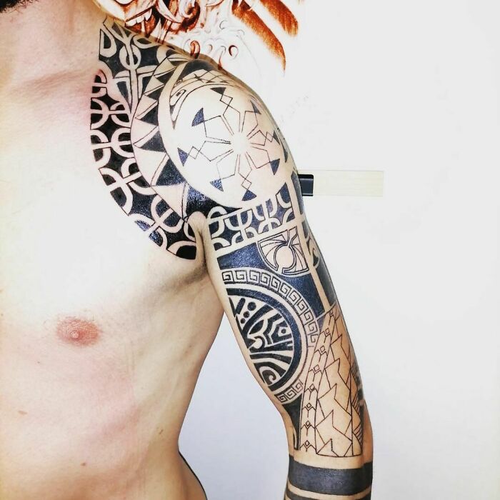 Intricate tribal tattoo design covering a man's shoulder and arm, showcasing bold geometric patterns.