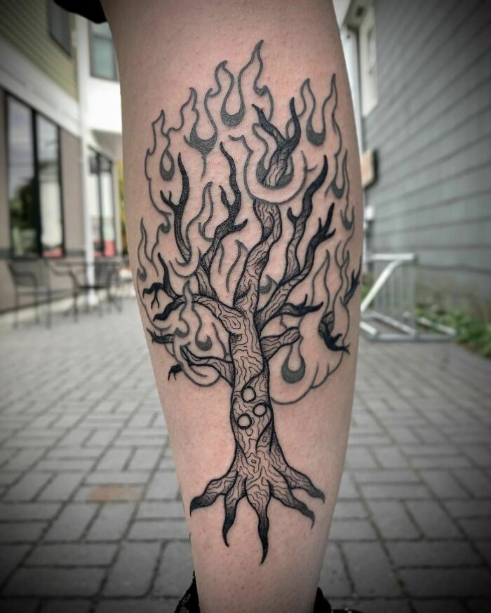 Tribal tattoo of a tree with flame-like branches on a leg in an urban setting.