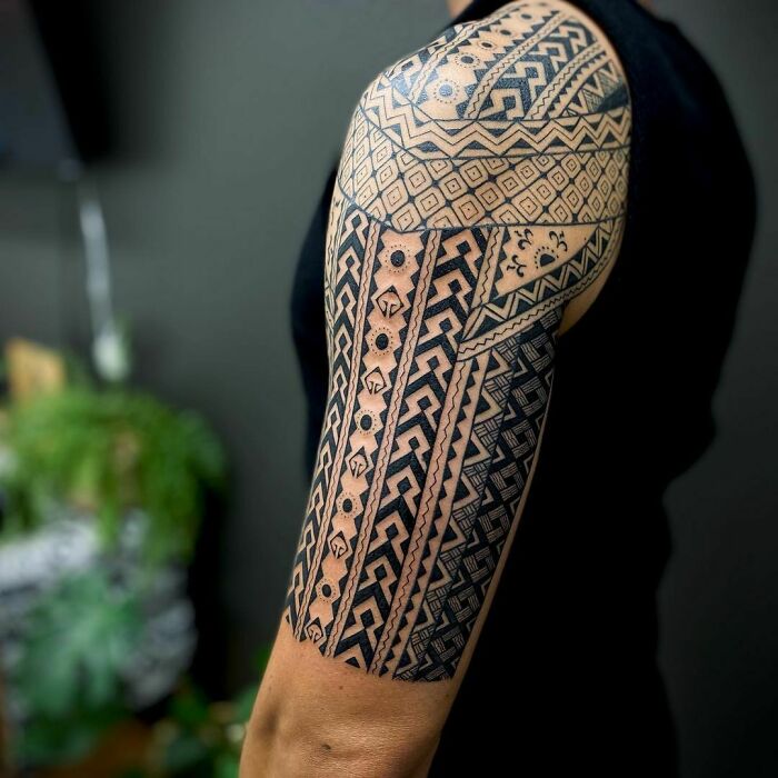Intricate tribal tattoo design on a person's upper arm, featuring geometric patterns and bold lines.