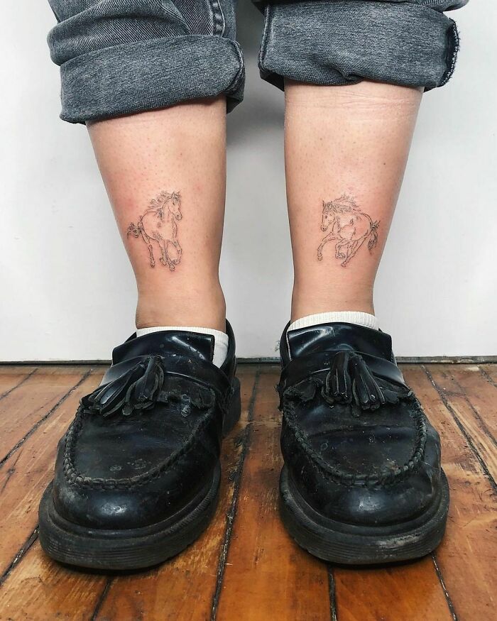 Ankle tattoos of running horses, worn with jeans and loafers on wooden floor.