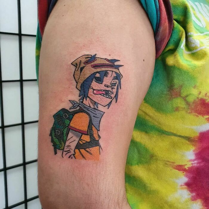 Pop culture tattoo of an animated character on an arm, featuring colorful design with tie-dye shirt background.
