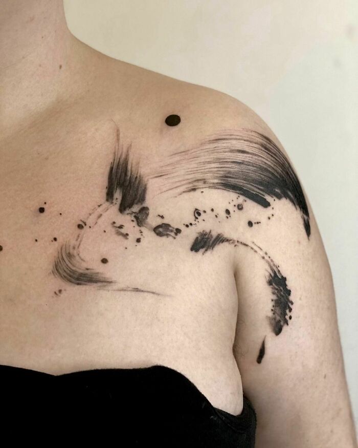 Abstract brushstroke collarbone tattoo design on a person's shoulder and upper chest.