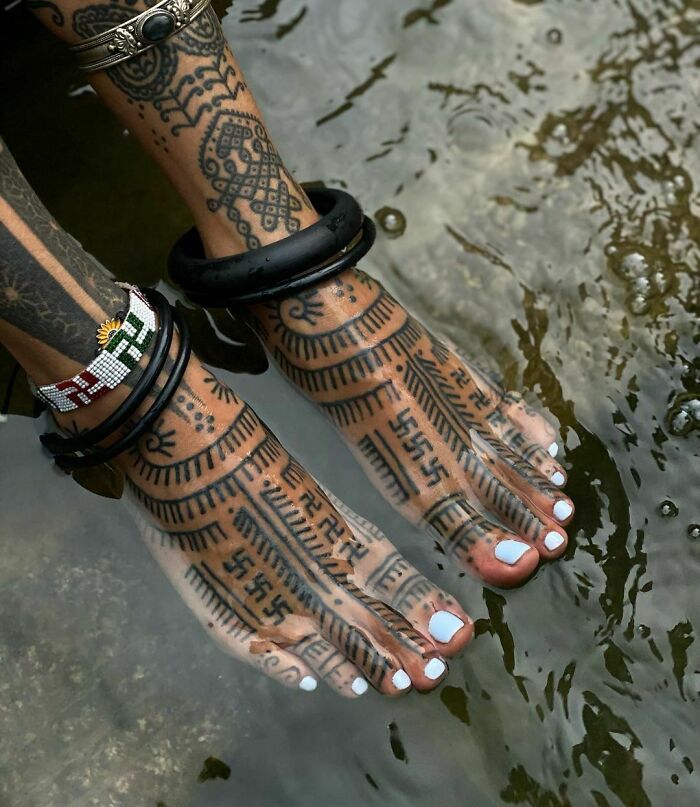 Feet with intricate tribal tattoos submerged in water, showcasing bold geometric designs and patterns.