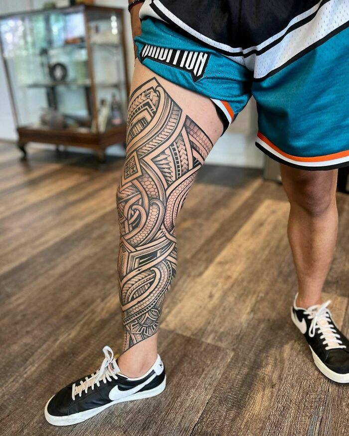 Person wearing shorts showcasing a detailed tribal tattoo on their leg.
