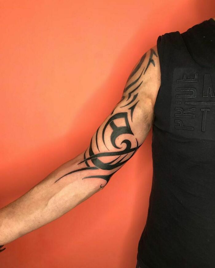 Arm with a bold tribal tattoo design against an orange background.