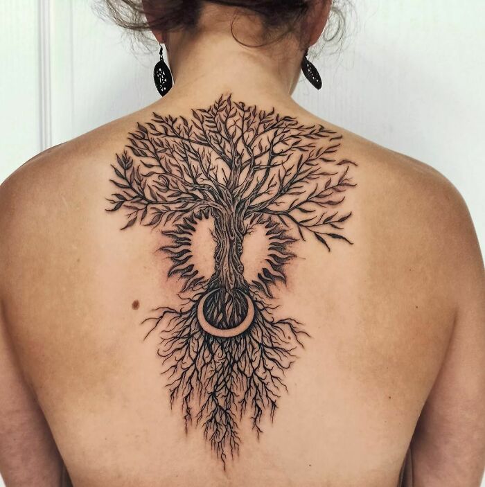 Back adorned with a large, detailed tree tattoo showcasing its branches and roots, celebrating the wonders of nature.