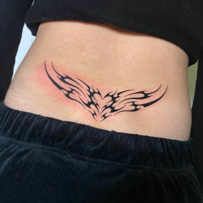 Lower back tribal tattoo with intricate design on a woman wearing black pants.