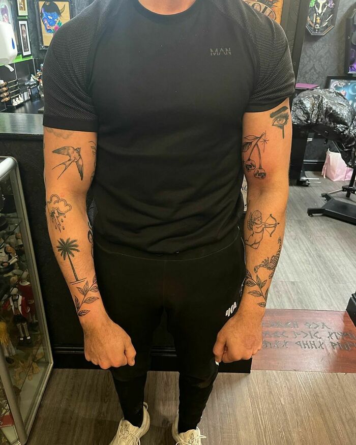 Man with patchwork tattoos on both arms standing in a tattoo studio.