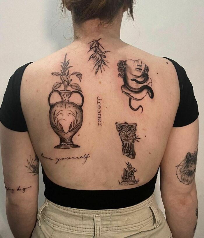 Woman's back showing creative patchwork tattoos with a vase, face, and inspirational words in various styles.