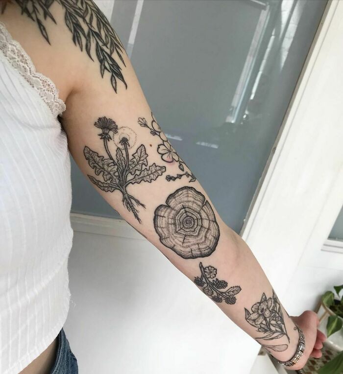Arm displaying intricate patchwork tattoo with floral and tree ring elements, showcasing unique tattoo artistry.