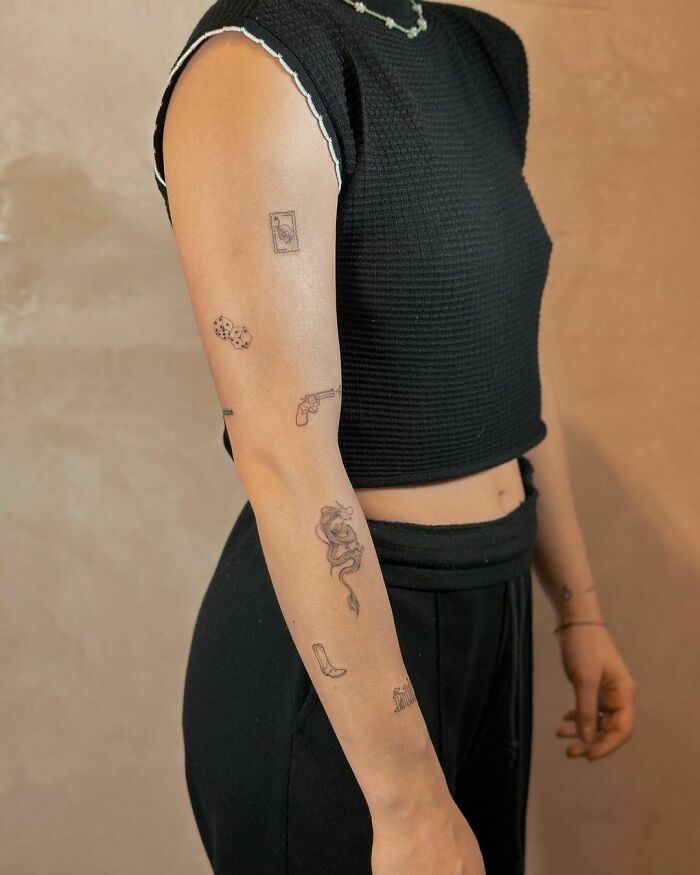 Person with patchwork tattoo art featuring dice, gun, and rose designs on arm, wearing a black sleeveless top.