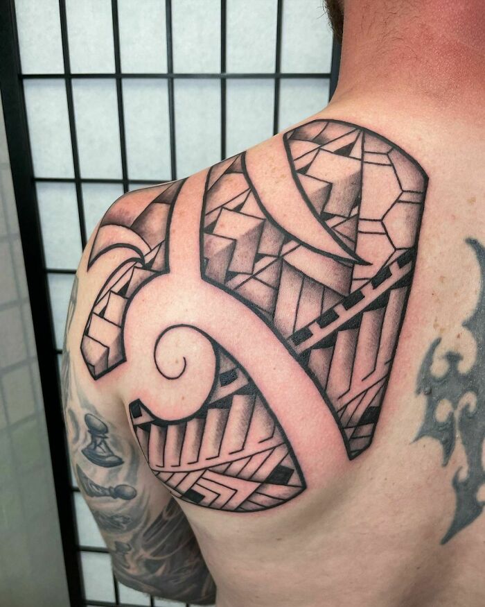 Black geometric tribal tattoo on a man's shoulder, featuring intricate patterns and bold lines.