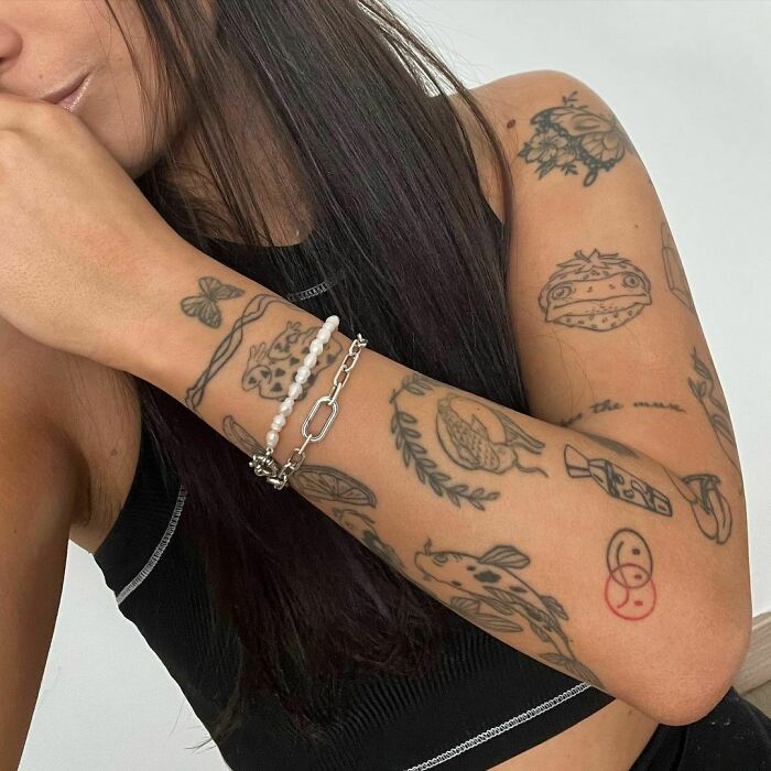 Person showcasing diverse patchwork tattoos on arm, including a koi fish and flowers, wearing a black tank top.