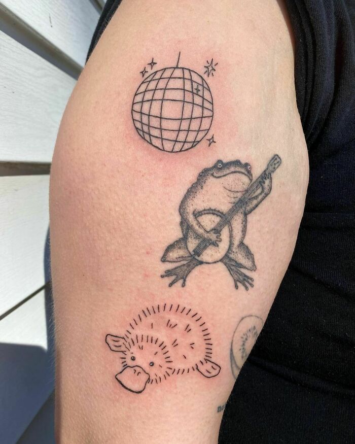 Patchwork tattoos on arm featuring a frog with a banjo, disco ball, and platypus design.