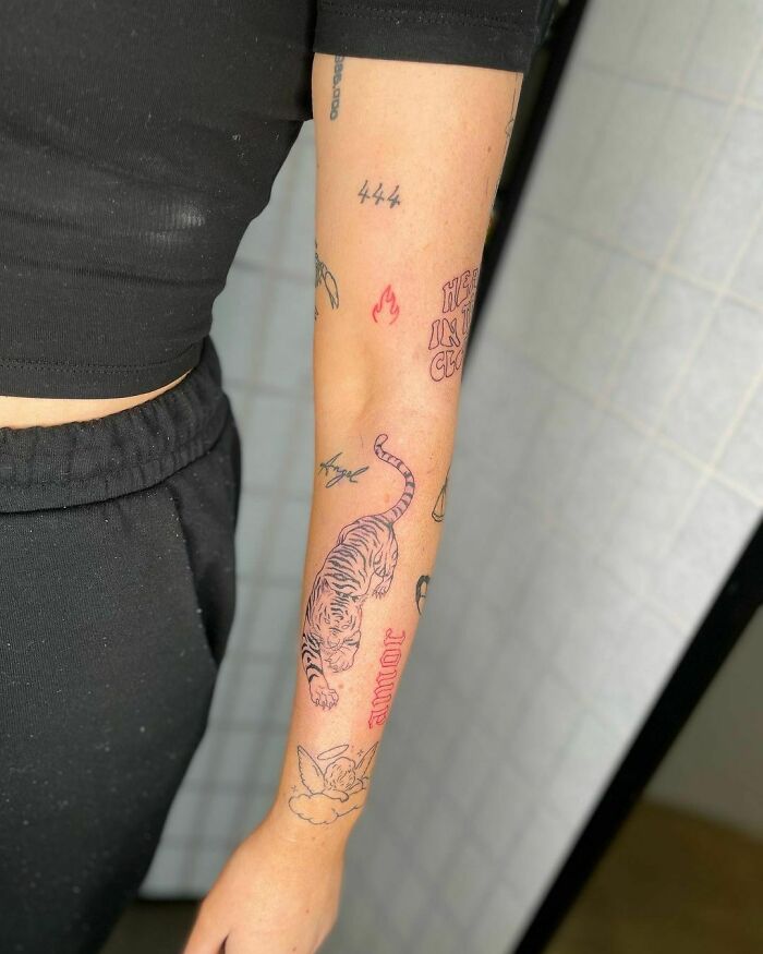 A forearm with various patchwork tattoos including a tiger, text, and small symbols, showcasing unique modern designs.