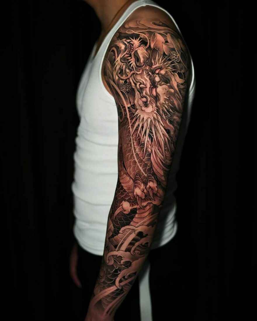 Arm displaying a detailed dragon tattoo in black ink, worn by person in a white tank top.