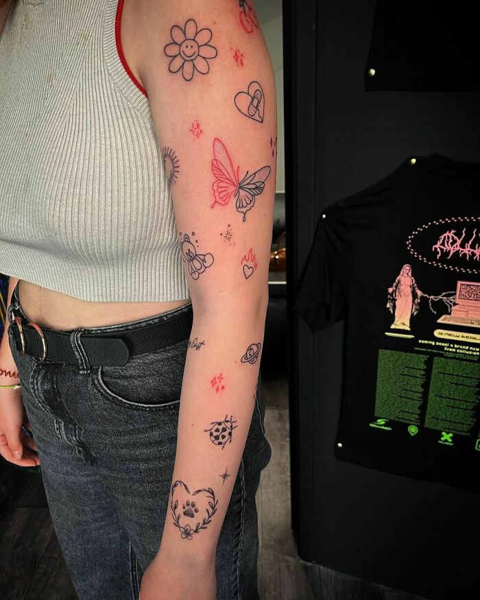 Person with patchwork tattoo sleeve featuring butterflies, flowers, and stars, wearing a gray tank top and jeans.