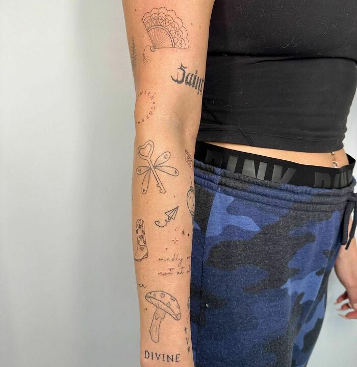 Arm featuring modern patchwork tattoos including text, mushroom, and fan designs, contrasting casual attire.