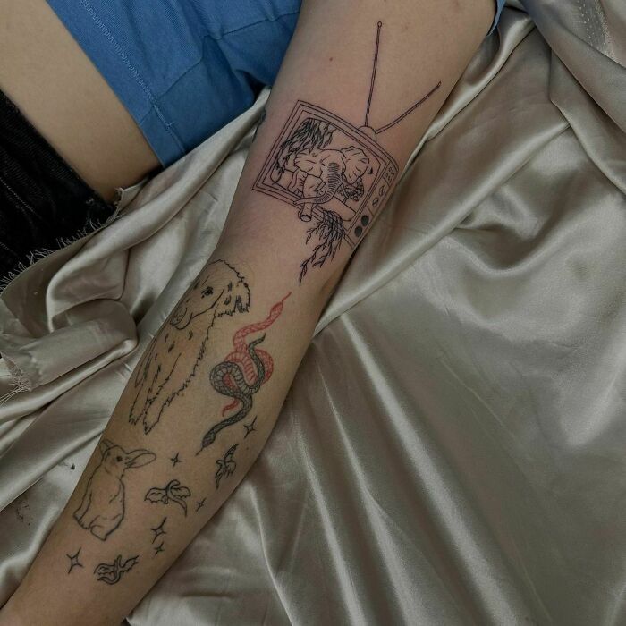 Arm showcasing patchwork tattoo designs with a dog, snake, and TV illustration on a silky fabric background.