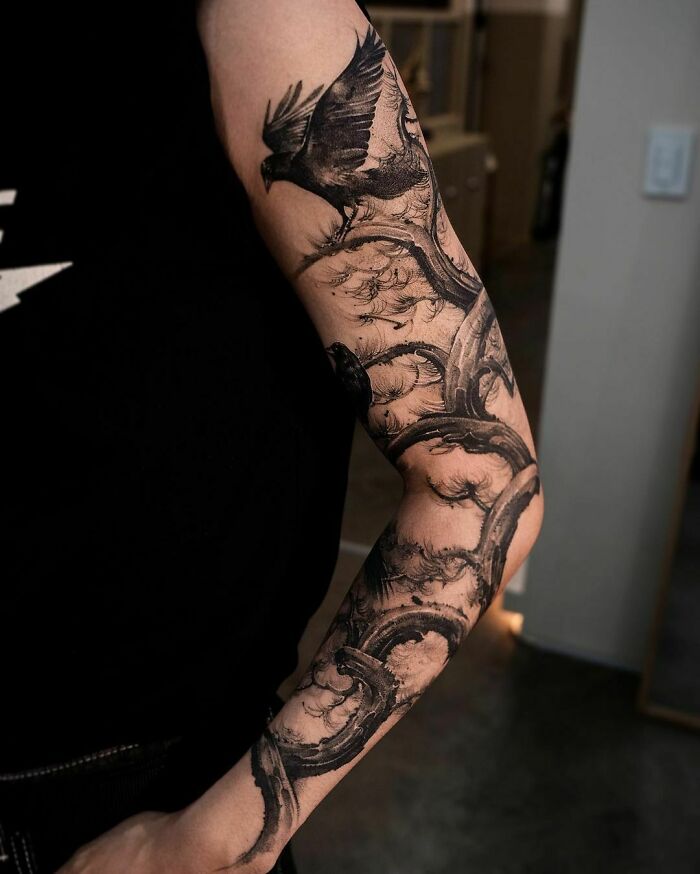 Arm adorned with a majestic tree tattoo featuring intricate branches and a soaring bird.