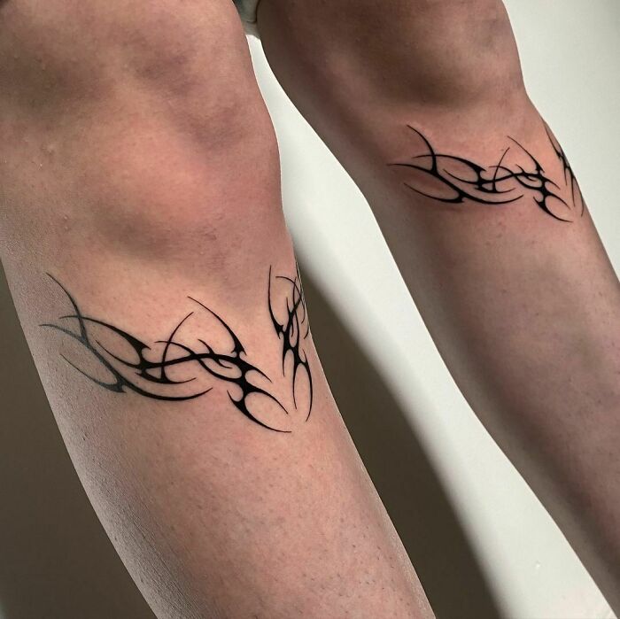 Tribal tattoos on legs with intricate black design and sharp angles, showcasing bold body art.