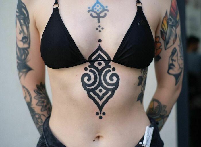 Woman with intricate tribal tattoo designs on arms and torso wearing a black bikini top.