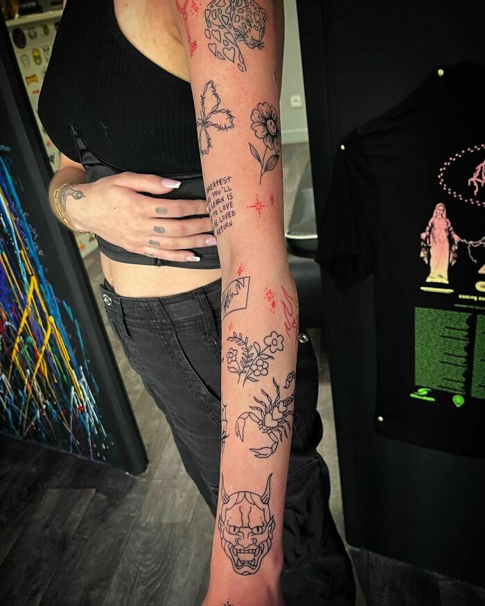 A person's arm covered in unique patchwork tattoos, featuring various designs like a leopard, butterfly, and Oni mask.