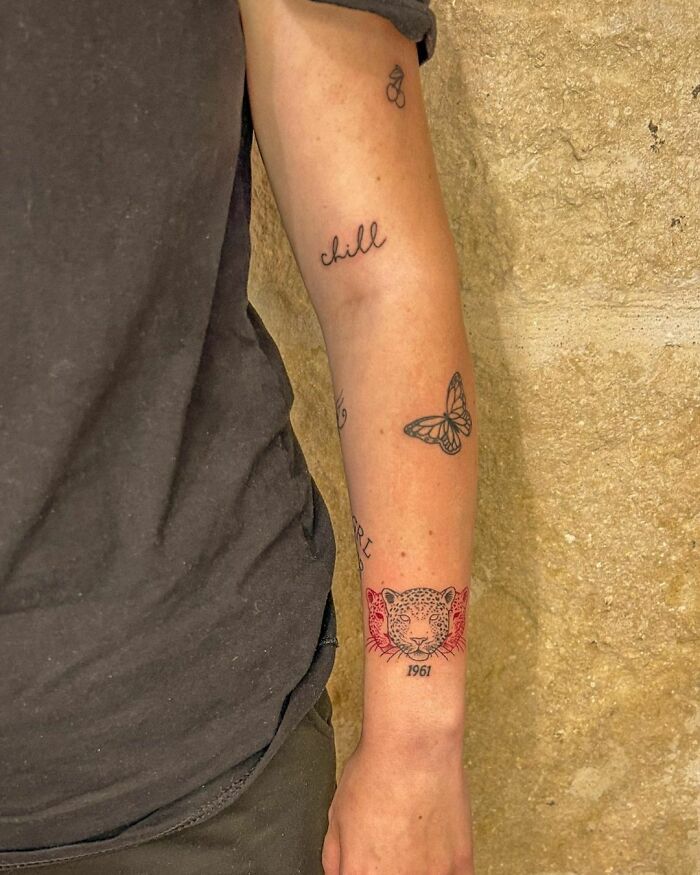 Arm featuring patchwork tattoos: a leopard head, butterfly, and "chill" text, showcasing modern ink designs.