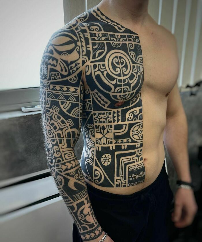 Man showcasing an intricate tribal tattoo sleeve extending to his chest.
