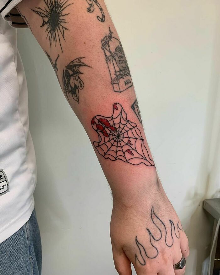 Arm featuring patchwork tattoo designs, including a spider web and flame pattern on the hand.