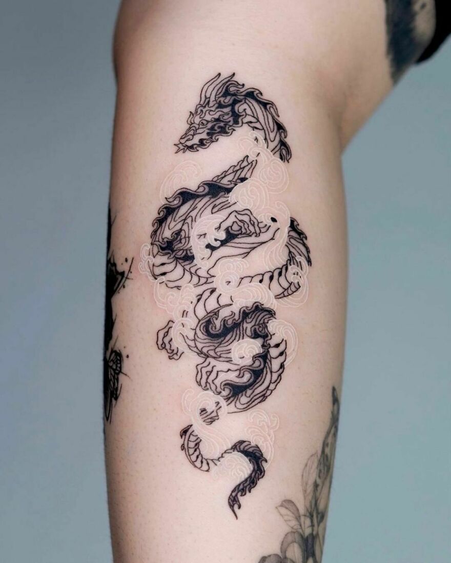 Intricate black and white dragon tattoo design on an arm, showcasing detailed scales and flowing mane.