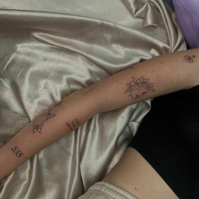 Arm with unique patchwork tattoos, including flowers and numbers, resting on satin fabric.