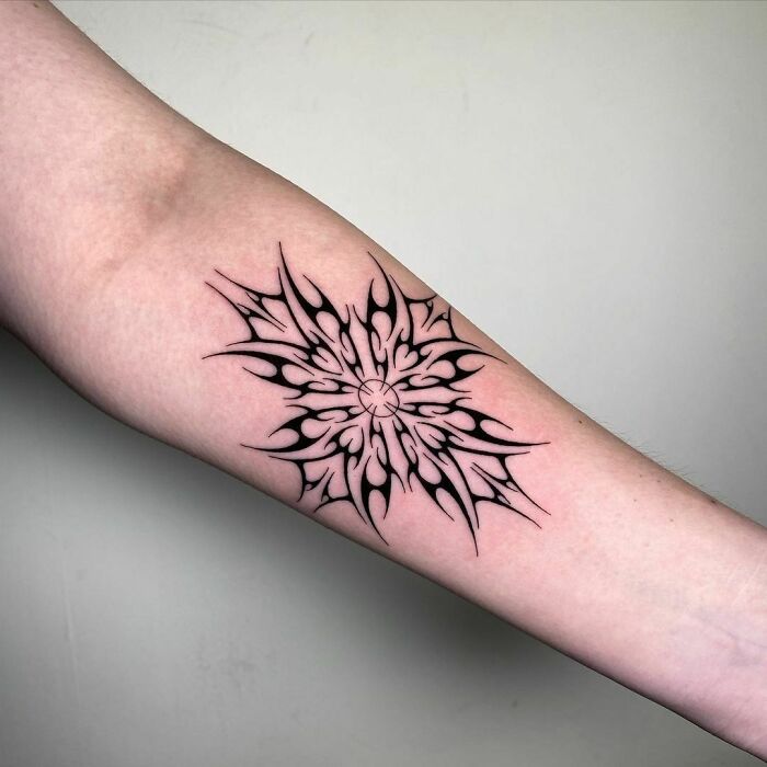 Intricate tribal tattoo design on a forearm, featuring symmetrical black patterns.