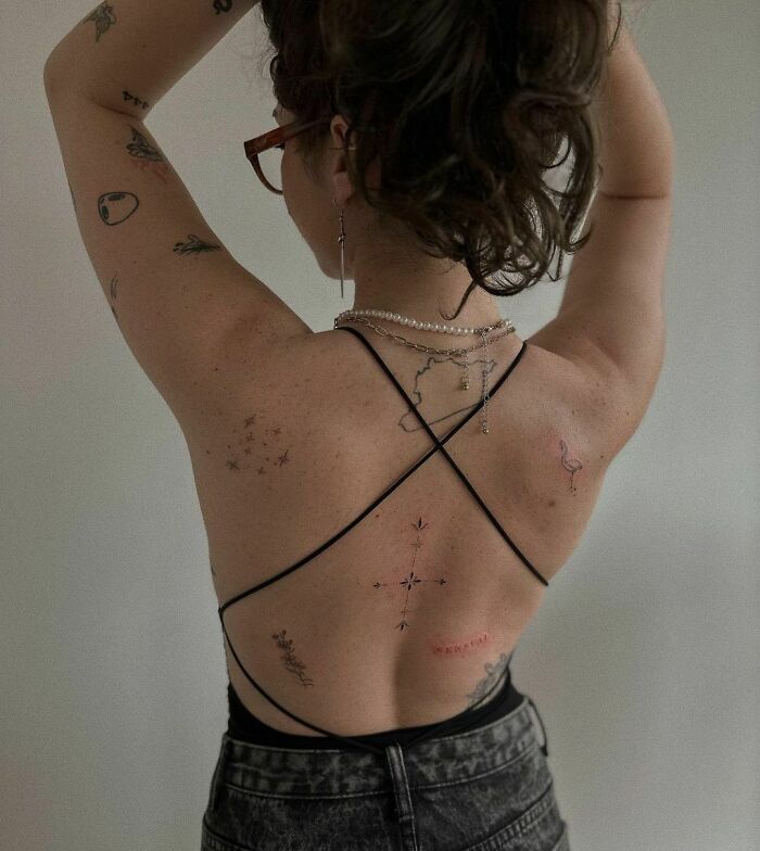 Back view of a person with multiple patchwork tattoos wearing a strappy top and necklaces.
