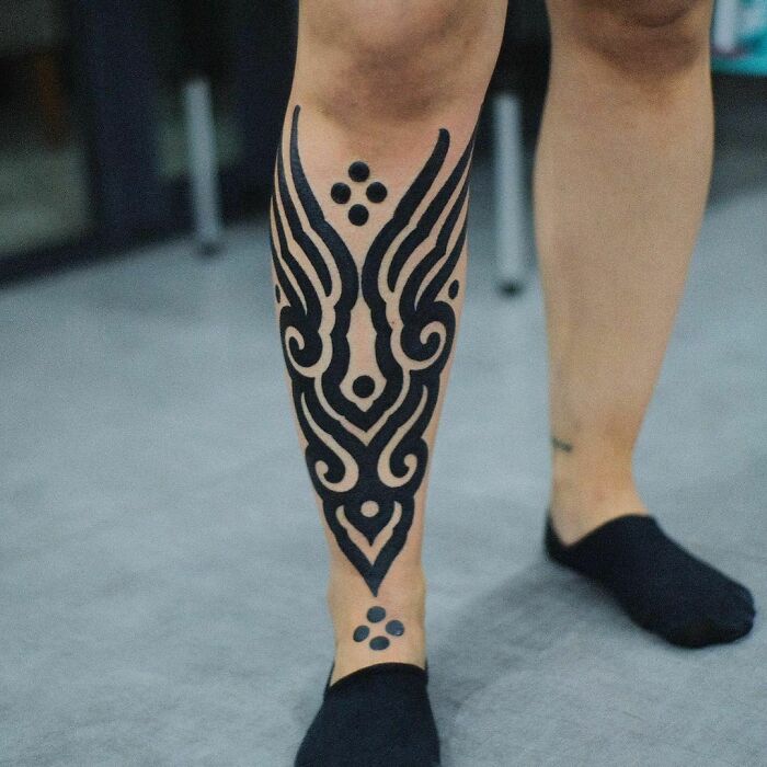 Tribal tattoo on leg with intricate black patterns, showing unique design and style inspiration.