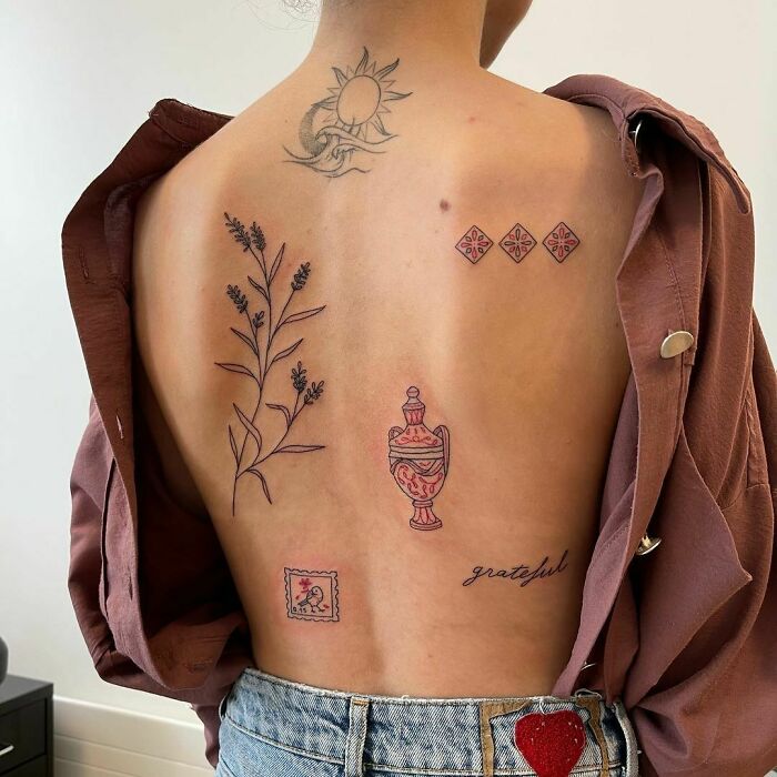 Person with patchwork tattoo designs, featuring a sun, floral, and script elements, wearing a brown shirt and jeans.