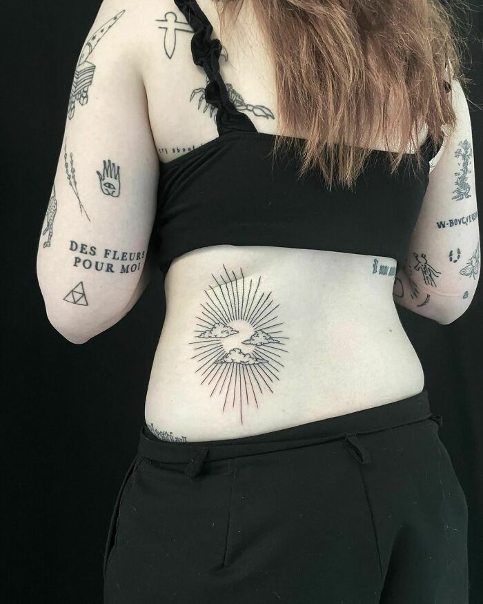 Person showcasing patchwork tattoos on their arms and back, featuring a sun and cloud design on the lower back.